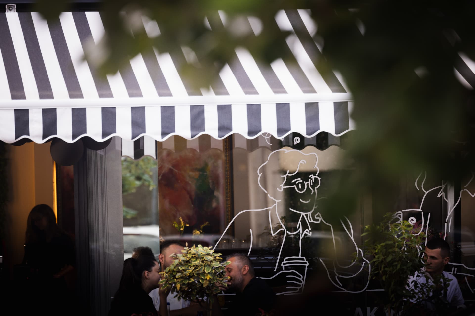 Guests at ENO-AD Coffee framed by green leaves outside the entrance